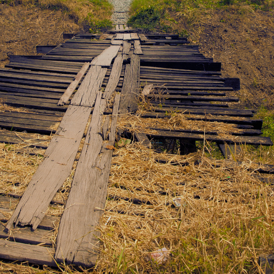 A rotting wooden bridge is repaired by adding new planks on top. This keeps the bridge in operation while increasing instability